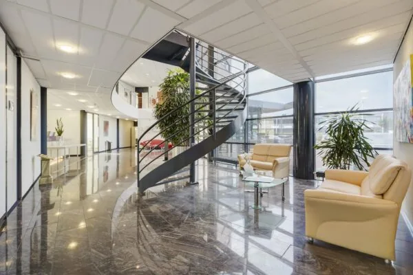 Moderne entreehal aan de Laan van s-Gravenmade met een glazen gevel, leren zitmeubilair en een centrale wenteltrap.